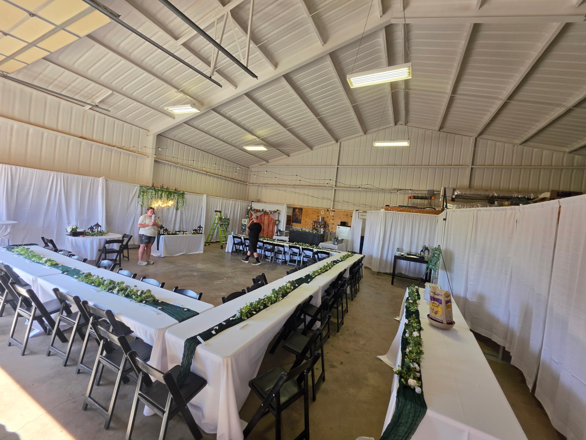 Barn reception setup with long farmhouse tables and greenery